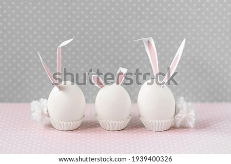White chicken eggs with bunny ears and tails on bed flowers background. A family. Happy Easter holiday concept.