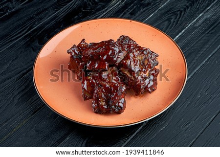Appetizing and juicy beef ribs in barbecue sauce, served in a plate on a dark background. American BBQ culture