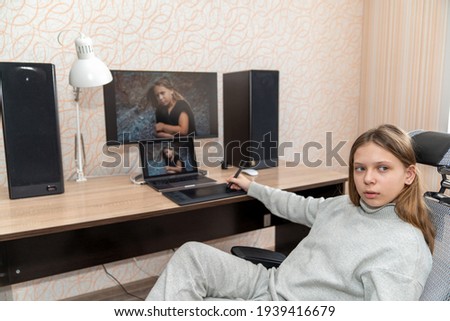 a girl sits at a computer table and processes her image in a photo editor