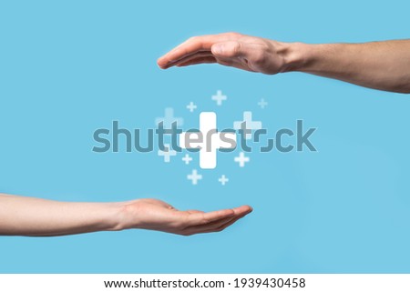 Male hand holding plus icon on blue background. Plus sign virtual means to offer positive thing (like benefits, personal development, social network)Profit,health insurance, growth concepts. Royalty-Free Stock Photo #1939430458