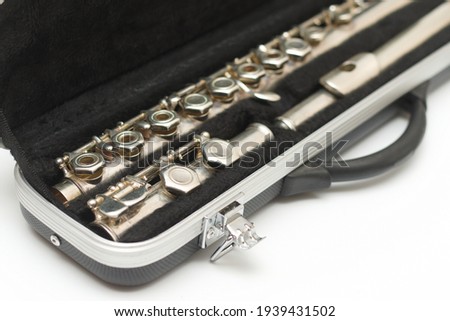 Partial side view of shiny disassembled silver flute in black case against white background