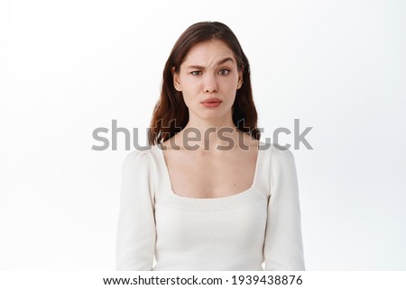 Confused young woman model raising eyebrow with disbelief, look doubtful at something strange, feeling unsure, standing against white background