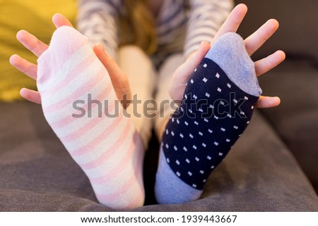 Down syndrome awareness concept. Girl wearing different socks while sitting on sofa at home. Different socks as symbol of down syndrome. Selective focus.