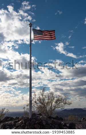 American flag waving on a desert mountaintop with clouds and a late afternoon sun