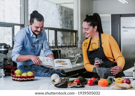mexican couple reading book with recipes while cooking mexican food in kitchen at home in Mexico city Royalty-Free Stock Photo #1939505032