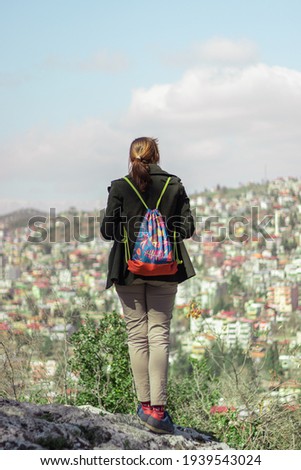 Brown hairy woman standing on a rock watching a beautiful village and mountains on a sunny day 