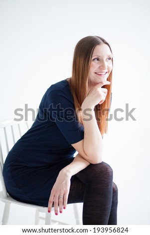 Studio portrait of happy smiling attractive woman wearing blue blouse and sitting in chair and holding hand to chin