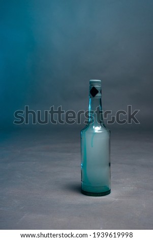 A bottle of alcohol filled with smoke stands on a gray background with blue glare 