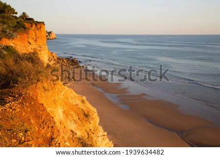 soft evening sunlight falls on the cliff wall and enhances the orange color of the sandstone, holiday makers and tourists walk along the coast on the beach or on the top of the mountain