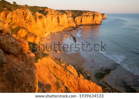 soft evening sunlight falls on the cliff wall and enhances the orange color of the sandstone, holiday makers and tourists walk along the coast on the beach or on the top of the mountain