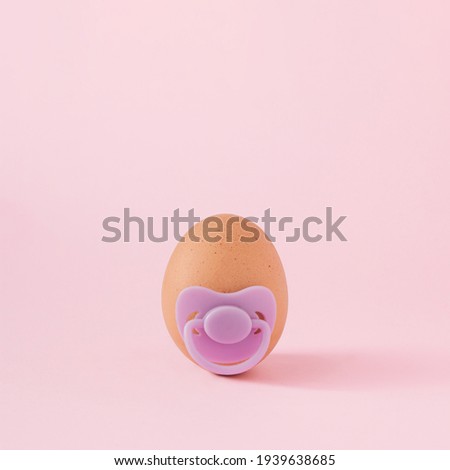 Natural egg with purple pacifier on pastel pink background. Minimal concept.
