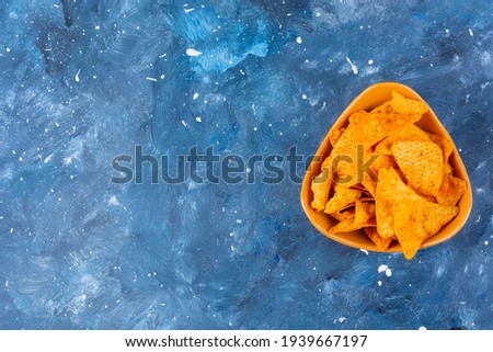 Details of pepper chips in orange bowl on colored blue table. High quality photo