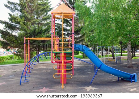 close-up colorful new playground with a slide and swings on a background of green trees in spring