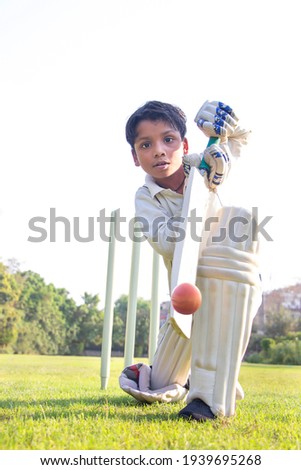 Young boy batting in protective gear during a cricket Royalty-Free Stock Photo #1939695268