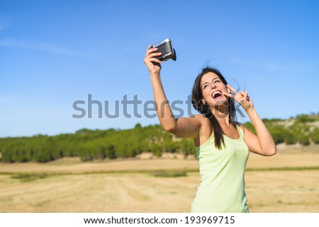 Brunette woman on summer vacation trip taking selfie photo with retro camera and having fun. Female traveler enjoying countryside in Spain.