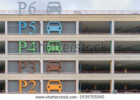 large parking lot construction with coloured floor signs and red metal handrails under grey cloudy sky in summer