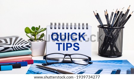 Against the background of a blue scheme and a white wall, black pencils in a stand, a flower, diaries and a notebook with the inscription QUICK TIPS