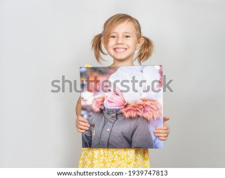 A Little Caucasian girl holding a photobook with her photographs in her hands, advertisement posing against studio wall. Advertising concept