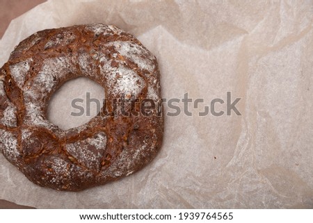 photograph of a round black cereal bread with a hole in the center on light craft paper for baking 