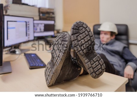 There is a close-up of the soles of the boots on the work table. The engineer put his feet on the table and is resting. Selective focus