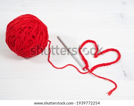 Red yarn clew with a knitting hook and a heart on a white wooden background. Copy space. Royalty-Free Stock Photo #1939772254