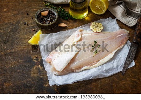 Seafood, raw white fish fillet for cooking. Fresh fillet Pangasius with spices, lemon and thyme on rustic wooden table. Copy space.
