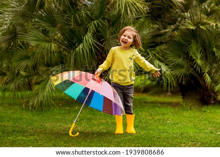 a beautiful girl in a yellow sweater and yellow boots, walking in the park with a colored umbrella, on a spring day
