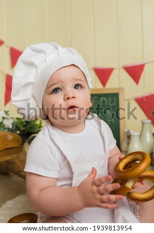 portrait of a baby girl in a chef's hat holding a bagel on a background with cooking