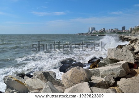 Photography of the waves breaking against a breakwater at Mar del Plata City during summertime whit the skyline on the background
