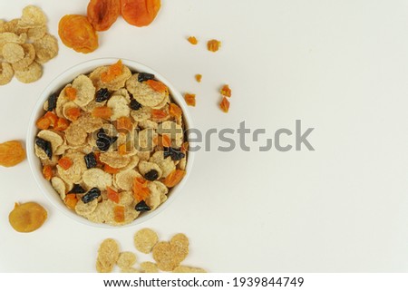 A bowl of cornflakes with dried apricots and prunes, top view. White background