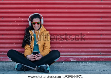Girl in yellow raincoat listening to music leaning on a red wall