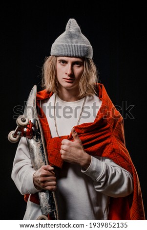Portrait of a stylish man holding a skateboard in the Studio. Close-up of a smiling skateboarder posing on a black background.