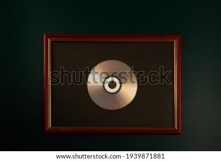 Silver CD in a wooden photo frame on a dark background. Symbolic award.