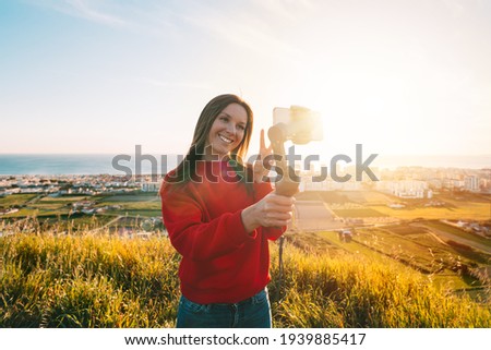 Woman vlogger holding gimbal with phone and taking selfie or live streaming outdoors at sunset. Taking pictures and live video. Blogging. High quality photo Royalty-Free Stock Photo #1939885417