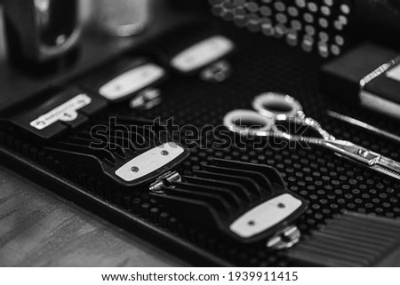 Black and white photo, selective focus, graininess, hairdressing items (nozzles for hair clippers, combs, scissors, hairdresser) are placed on the table before the haircut