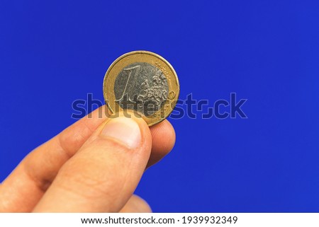 Hand hold one euro coin on a blue isolated background, close-up photo