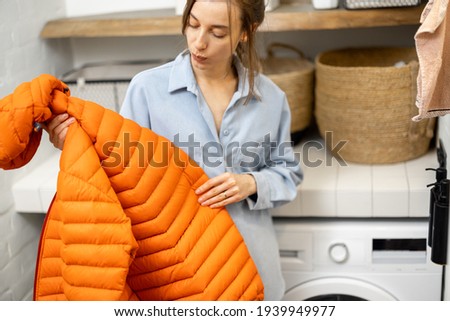 Young housewife looks on a down jacket before washing Royalty-Free Stock Photo #1939949977