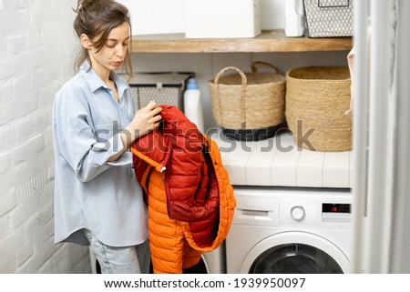 Young housewife looks on a down jacket before washing Royalty-Free Stock Photo #1939950097