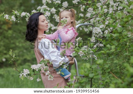 Mom and little daughter in white flowering branches of apple trees in spring