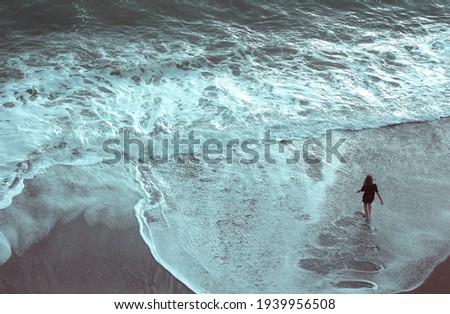 A woman stands alone  in front of a large tidal wave going to the beach in a storm 