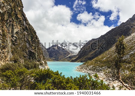 Beautiful view of the Parón lagoon with the snow-capped Pirámide de Garcilazo, Cordillera Blanca, surrounded by mountains, rocks and some trees in Caraz.