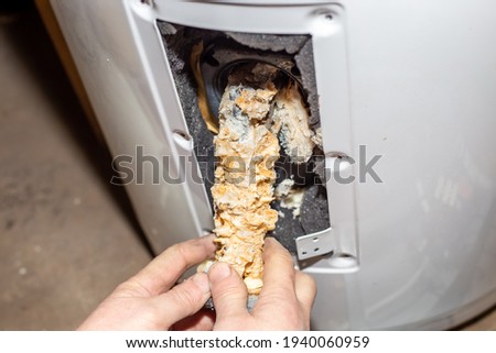 Repair and maintenance of boilers. The master plumber pulls out a tubular electric heater covered with lime scale from the hole in the boiler. Royalty-Free Stock Photo #1940060959