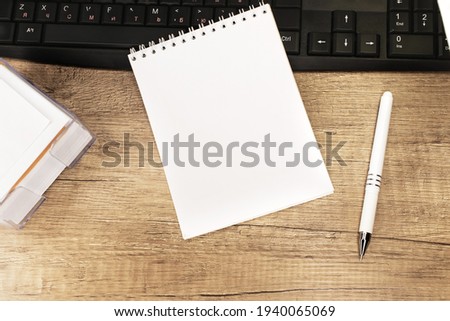 On a wooden table with a black keyboard is a notebook with a white blank sheet. Work and study online. Pattern