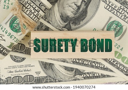 Business and finance concept. On the dollars is a wooden plate with the inscription - SURETY BOND Royalty-Free Stock Photo #1940070274