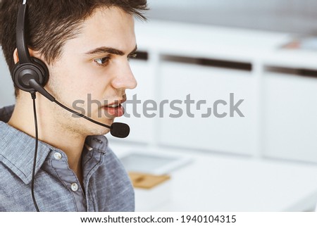 Casual dressed young man using headset and computer while talking with customers online. Call center, business concept