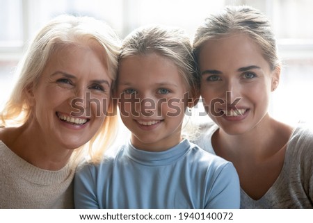 Close up headshot portrait of happy Caucasian three generations of women show family unity pose at home together. Profile picture of smiling little girl child with young mother and senior grandmother.