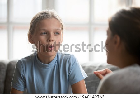 Small Caucasian teen girl child do articulation exercises with caring mother or teacher at home. Little kid pronounce sounds speak talk with tutor or coach, engaged in voice pronunciation together. Royalty-Free Stock Photo #1940142763