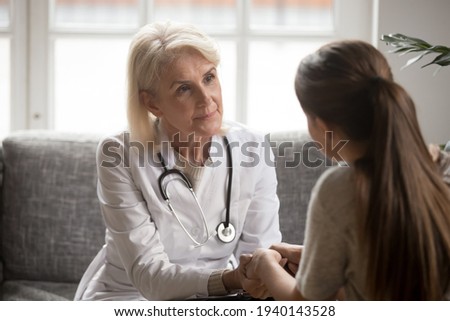 Attentive senior female doctor hold patient hands comfort support in difficult situation or illness. Caring woman GP or therapist feel supportive caress talk with client in hospital or clinic. Royalty-Free Stock Photo #1940143528