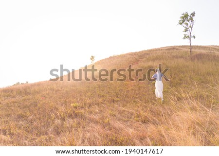 A woman dressed in a casual wedding dress Was running on the path of the barren brown grassland And has a background of small mountains And towards the sun Soft and warm backlighting