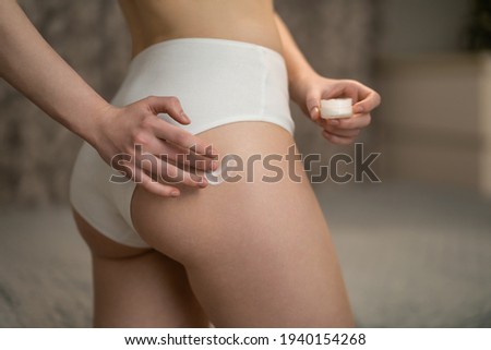 Body care. Woman applying cream on legs and buttocks. girl in a black thong, athletic. studio shot on a blue background. Royalty-Free Stock Photo #1940154268